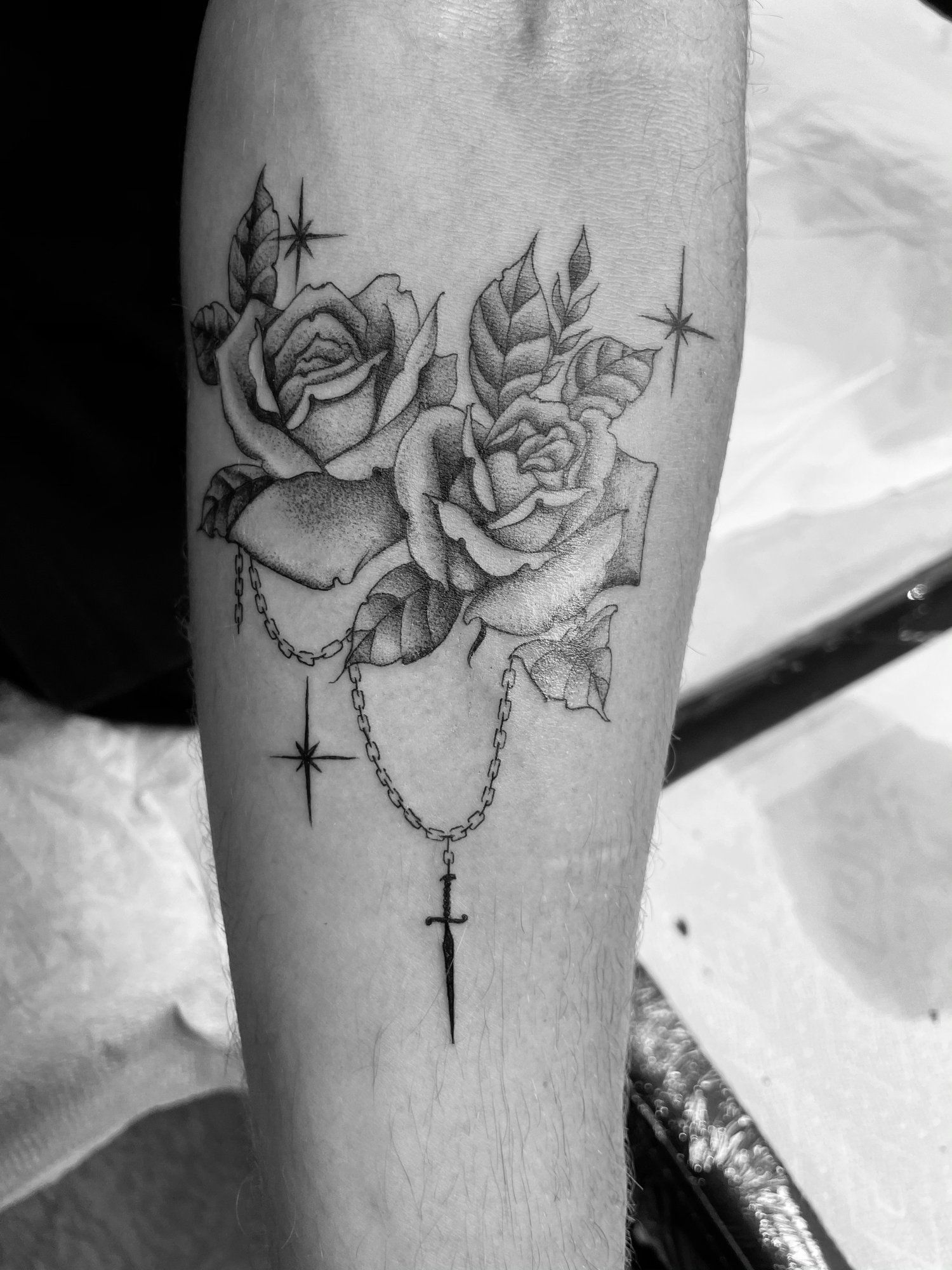 A black and white tattoo of roses and a rosary on a person 's forearm.
