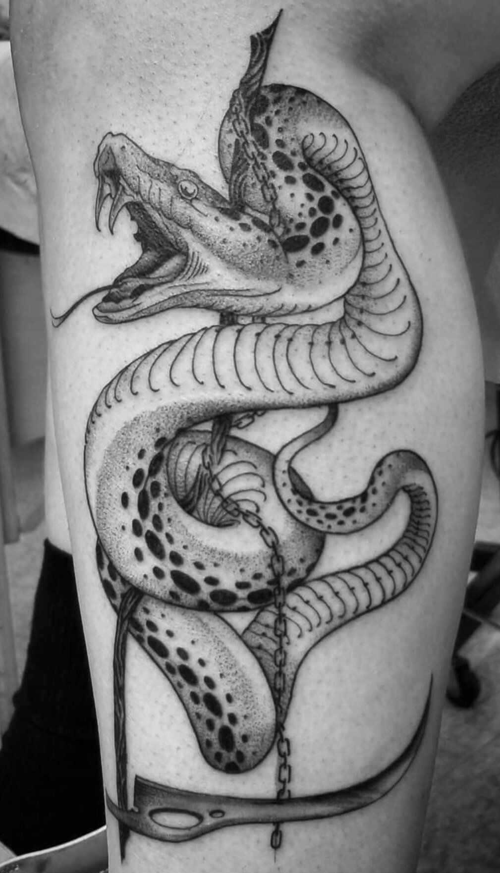 A black and white tattoo of a snake on a person 's leg