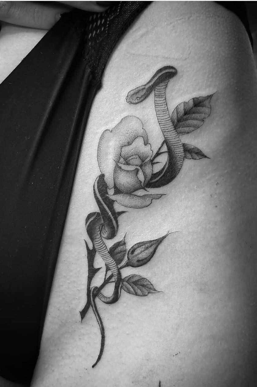 A woman has a tattoo of a rose and a snake on her thigh.