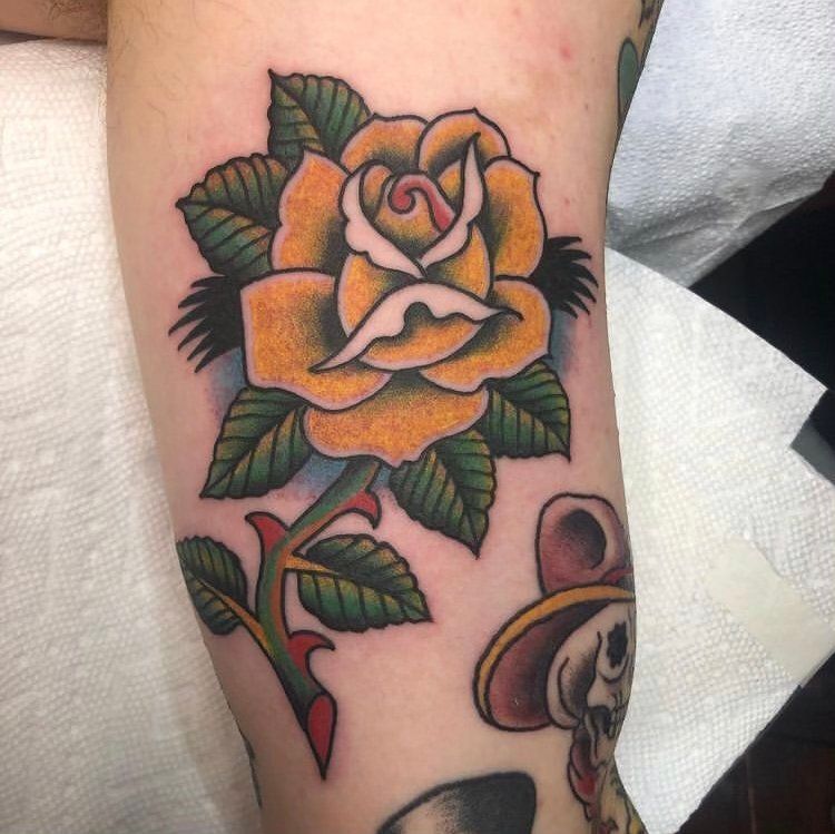 A person has a tattoo of a yellow rose on their arm