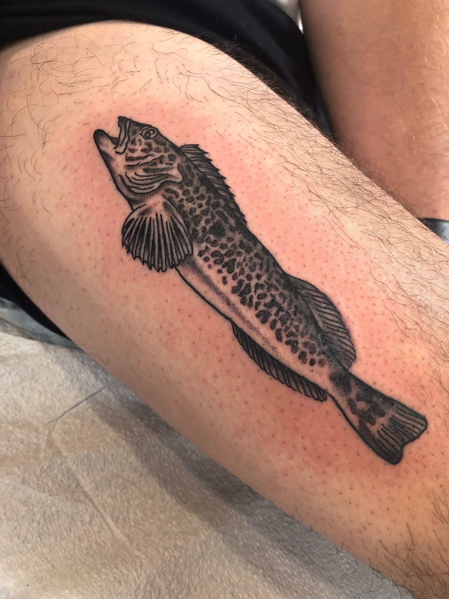 A man has a tattoo of a fish on his leg.