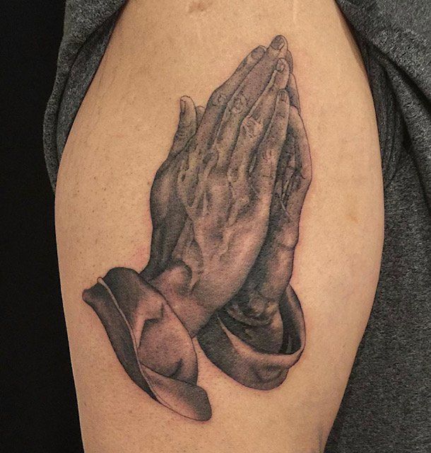 A person has a tattoo of praying hands on their arm