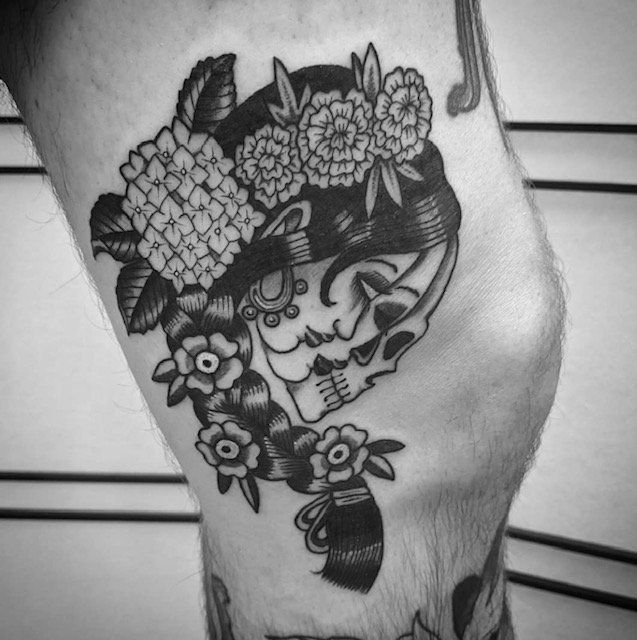 A black and white tattoo of a woman 's face with flowers on her head.