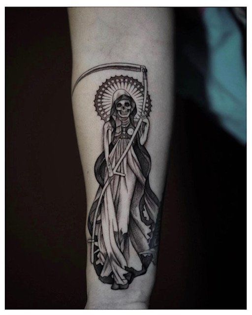 A black and white tattoo of a woman with a scythe on her arm.