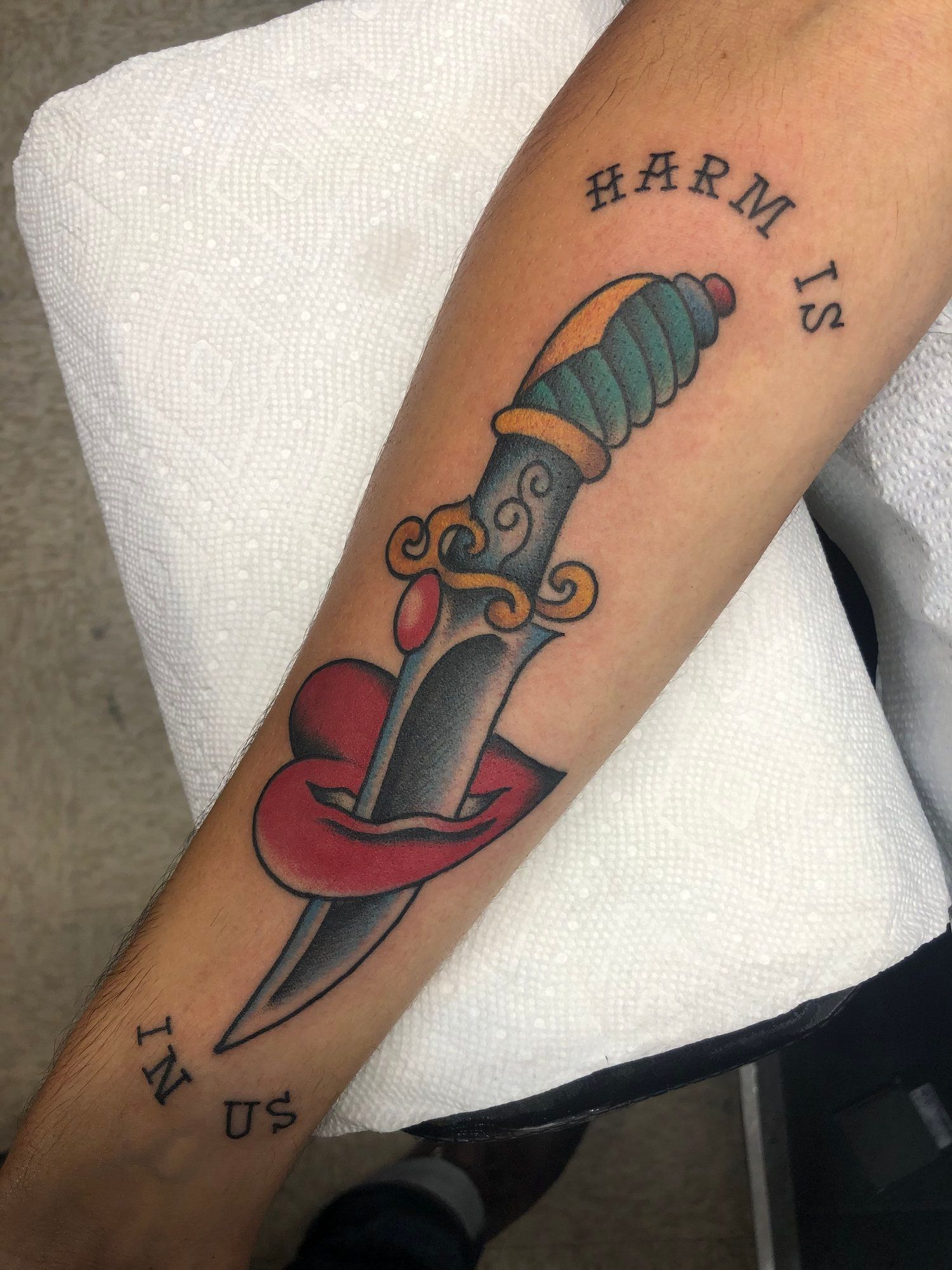 A person has a tattoo of a dagger on their forearm