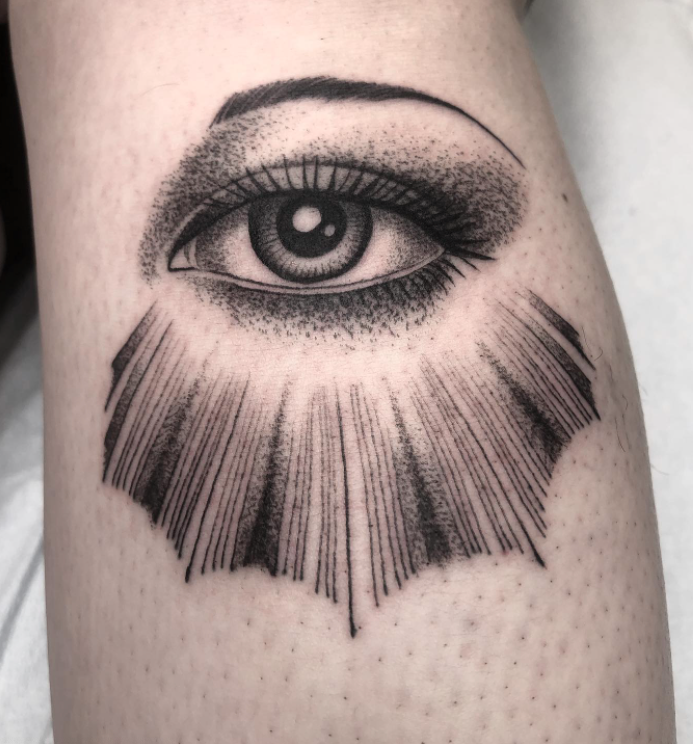 A black and white tattoo of an eye with rays coming out of it