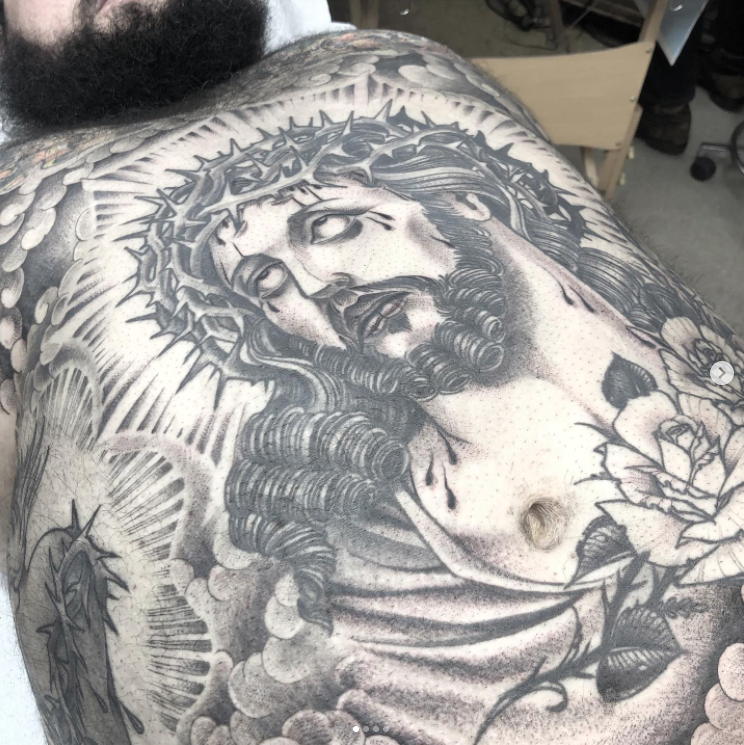 A man has a tattoo of jesus with a crown of thorns on his chest