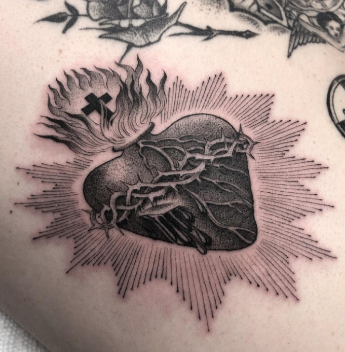 A black and white tattoo of a heart with thorns around it