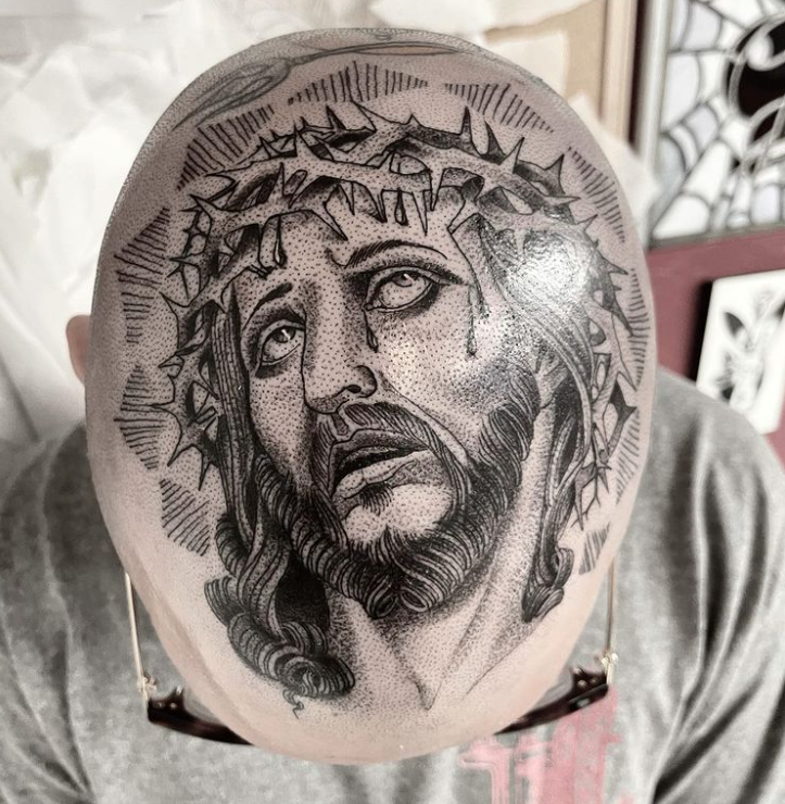 A man has a tattoo of jesus with a crown of thorns on his head.