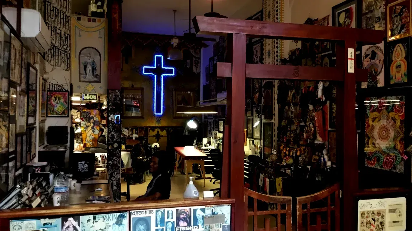 A neon cross is hanging from the ceiling of a tattoo shop.