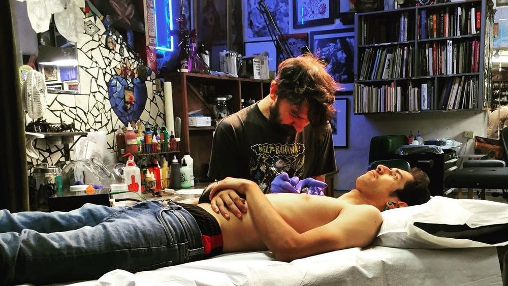 A man is laying on a bed getting a tattoo.