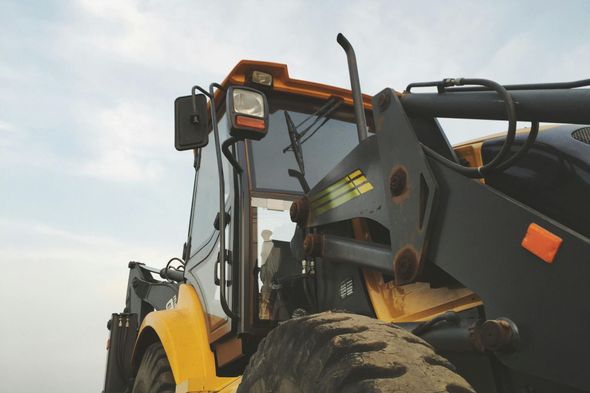 Close-up, low-angle view of a yellow construction vehicle, specifically a loader, against a cloudy sky.