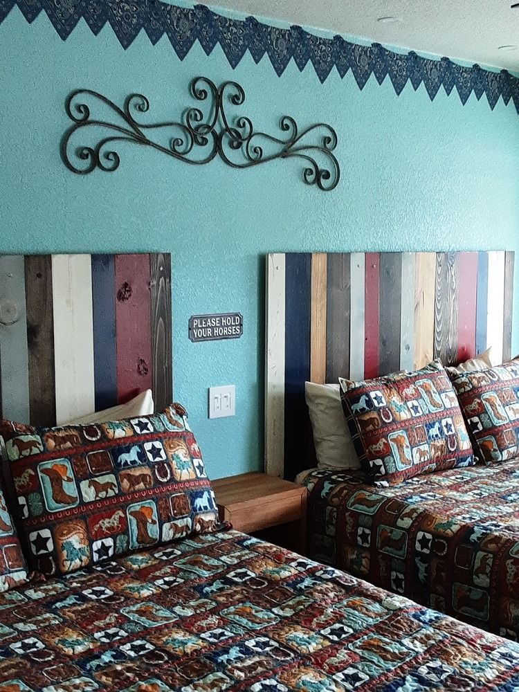 Two beds with rustic wooden headboards, turquoise wall, decorative scroll, and patterned bedding.