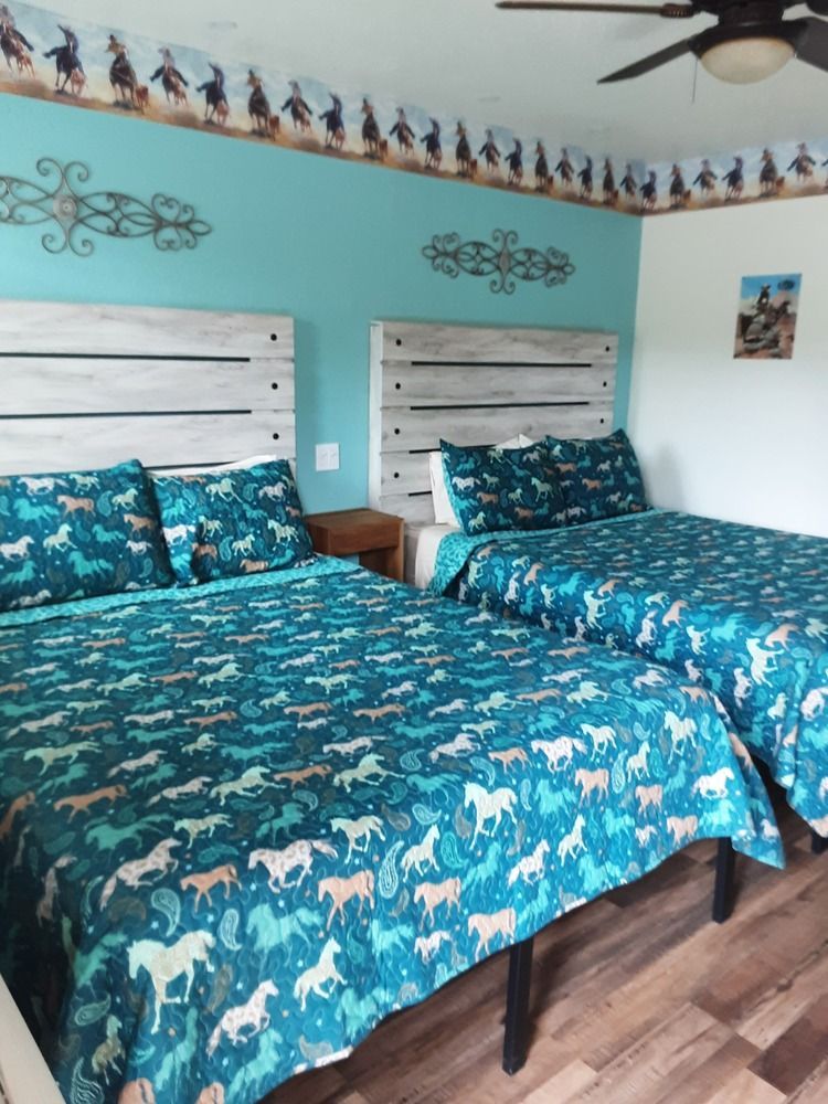 A room with two beds, turquoise walls and bedding, rustic headboards, cowboy themed wallpaper.