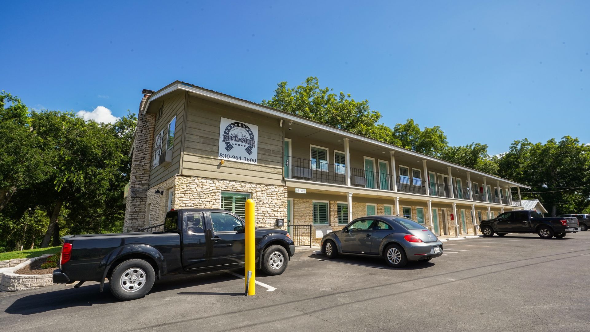 Motel with parking; a black pickup truck and gray car parked in front on a sunny day.