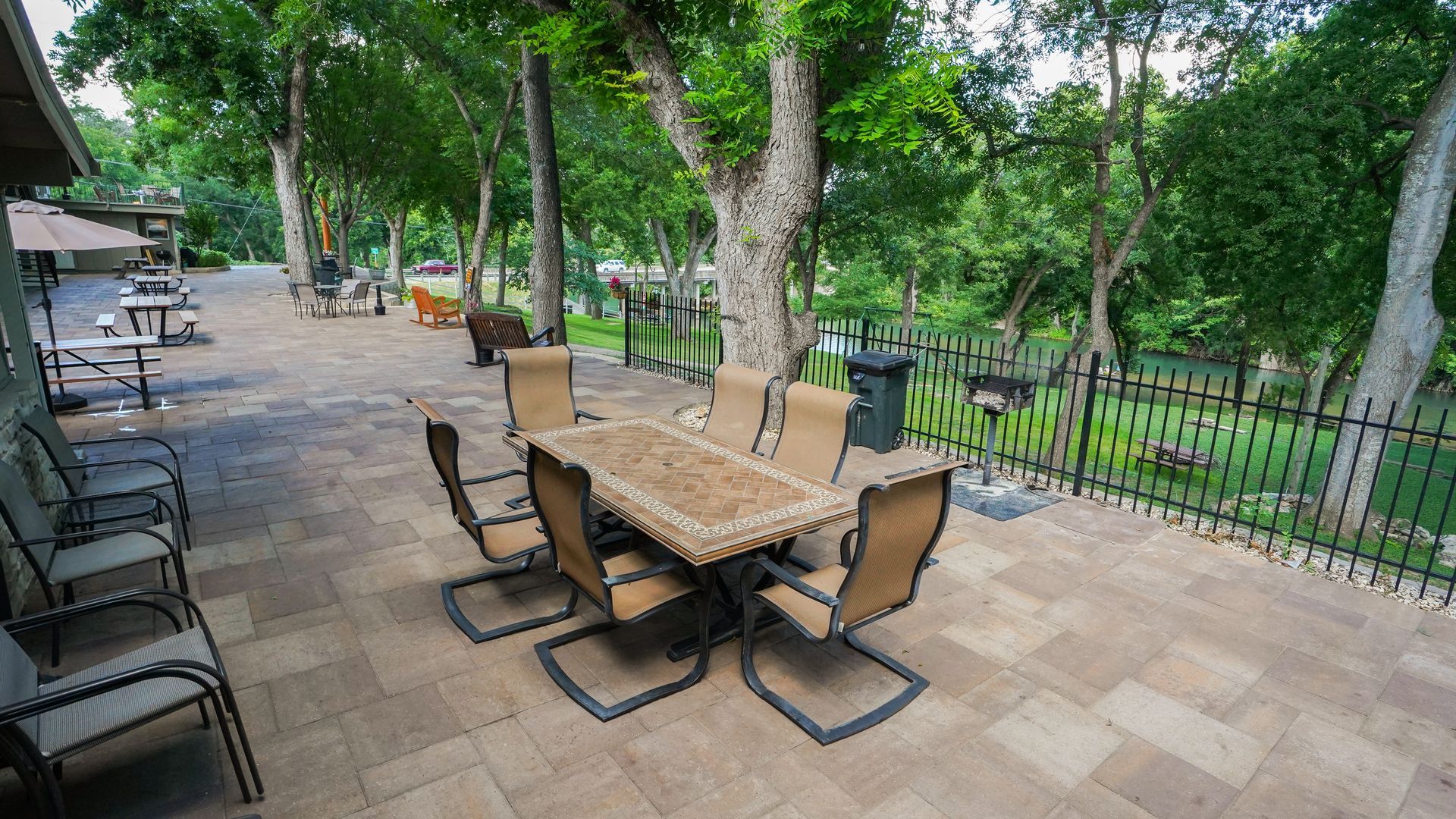 Patio with a table and chairs, surrounded by trees and a small fence, with a grill nearby.