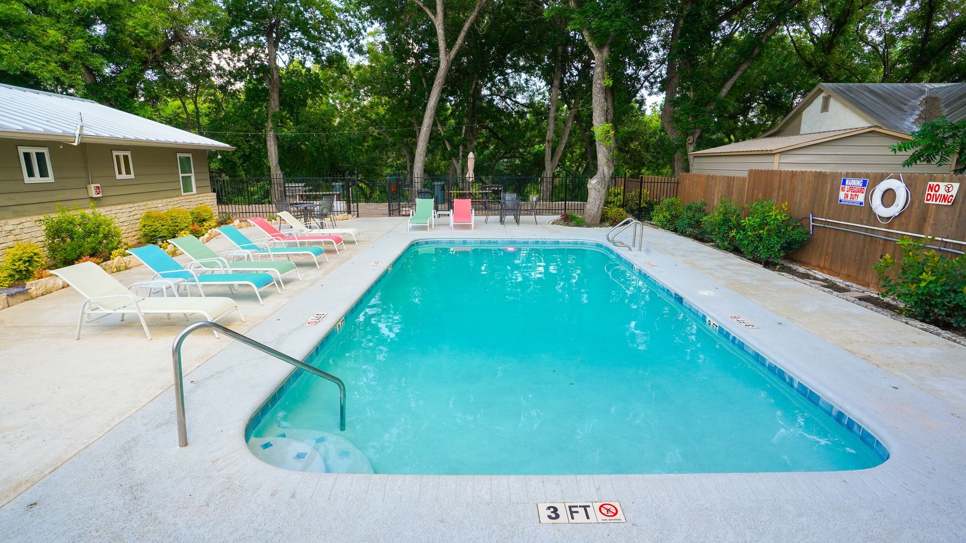 Pool with lounge chairs; trees in background.
