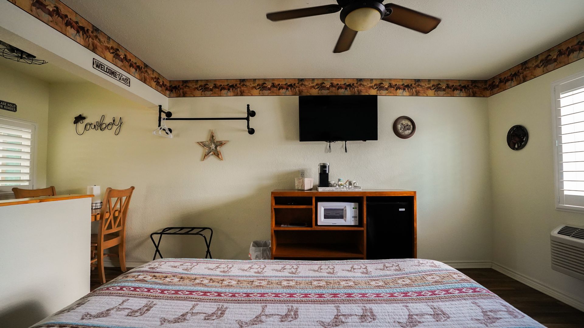Hotel room with bed, TV, microwave, and ceiling fan; floral border.