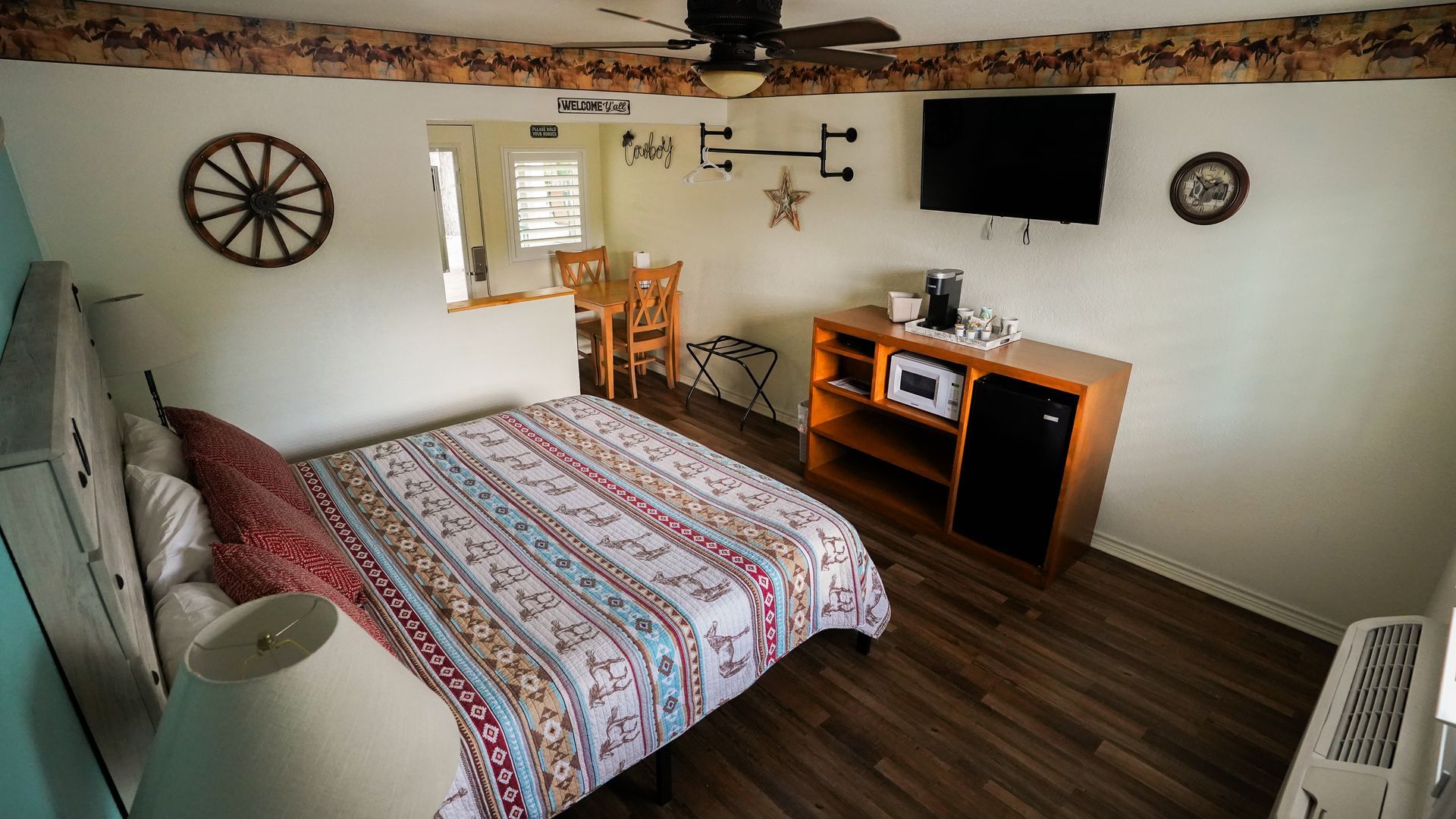 Bedroom with bed, TV, microwave, and table. Rustic decor includes wagon wheel, wood trim, and patterned bedding.
