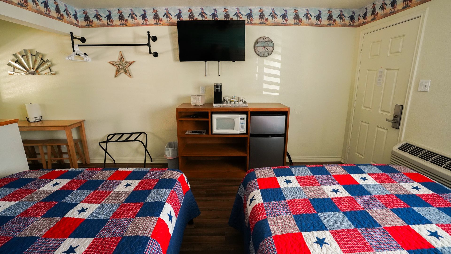 Two beds with patriotic quilts, a small room with a TV, fridge, and microwave.