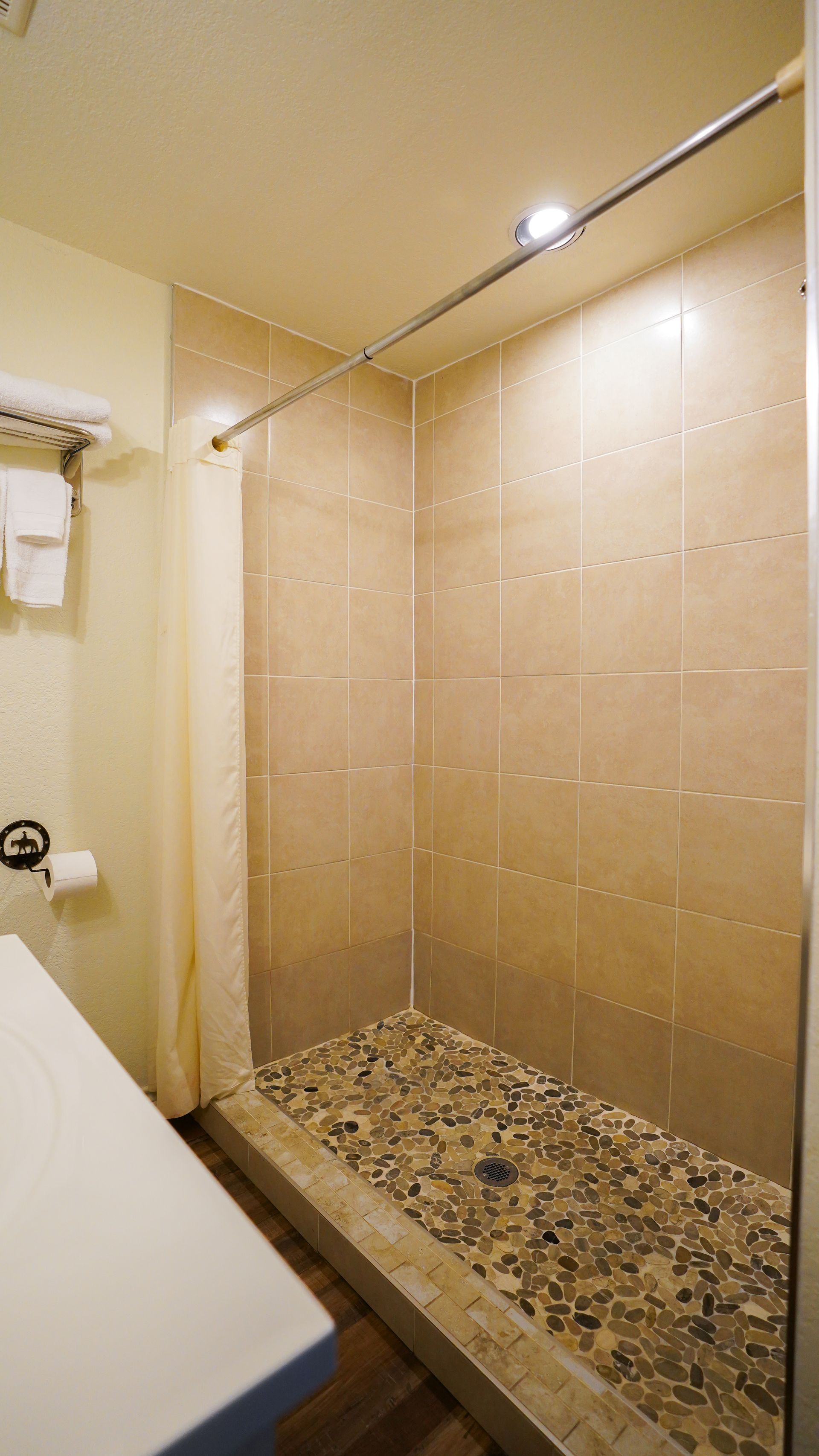 Shower with pebble-stone floor, beige tile walls, and a beige shower curtain.