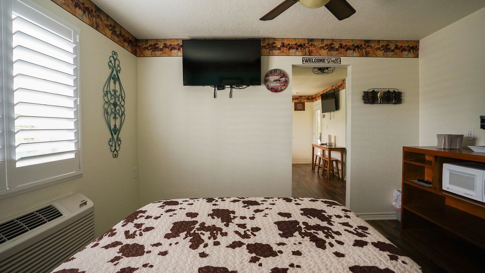 Bedroom with a cow-print bedspread, TV on wall, and an open doorway to another room.