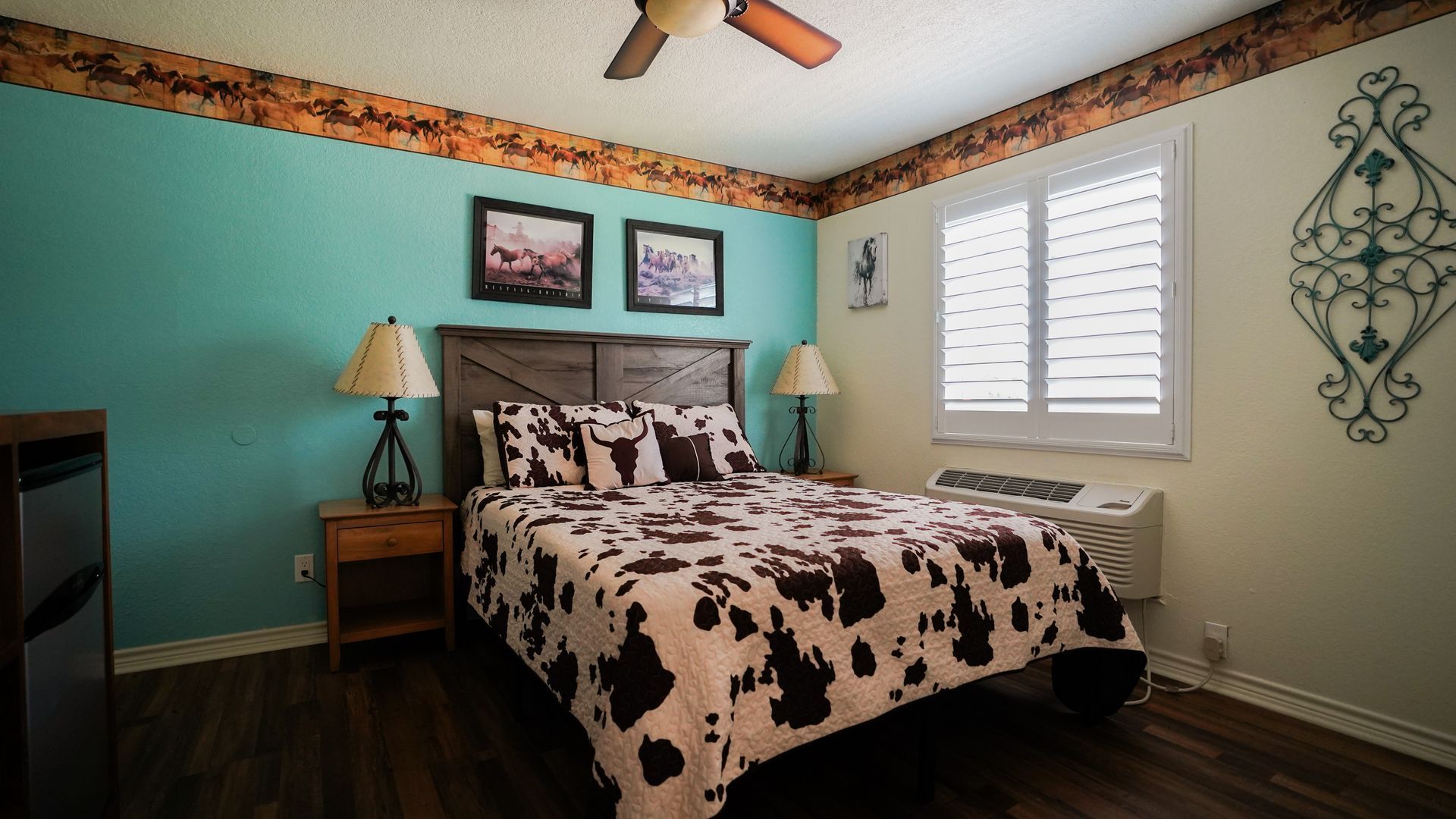 Bedroom with a cow print bedspread, teal wall, wooden furniture, and window with shutters.