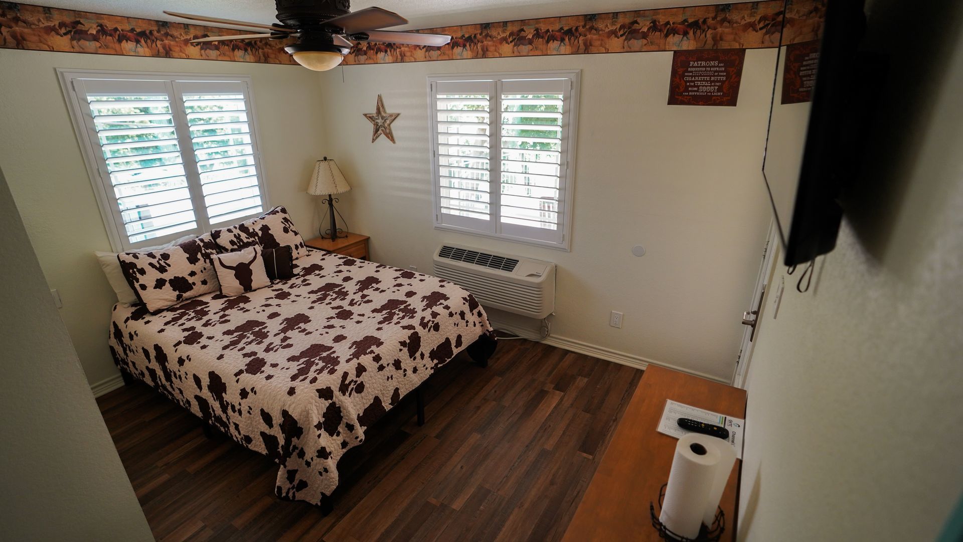 Bedroom with a cowhide-print comforter, two shuttered windows, and a ceiling fan.