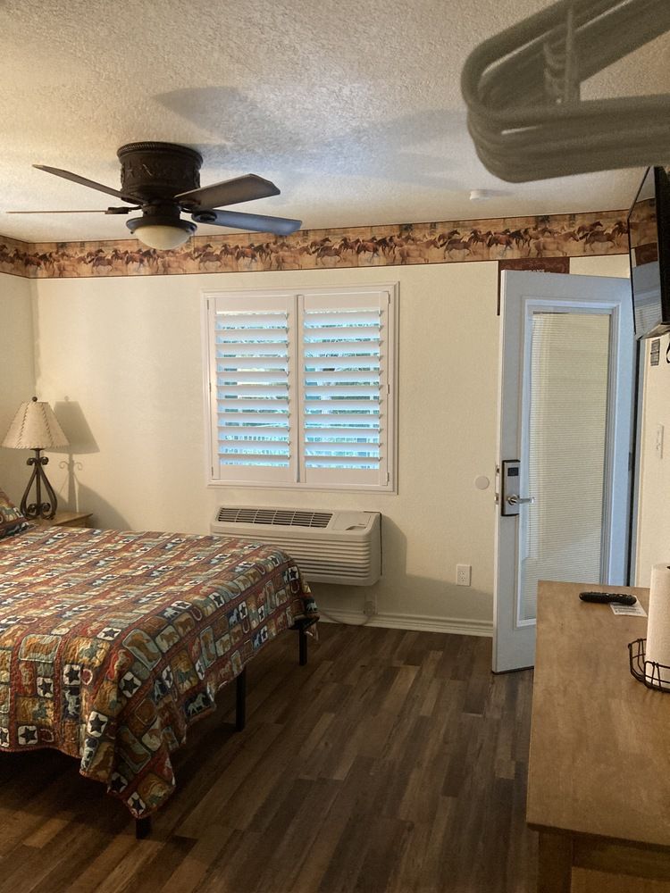 A hotel room with a bed, window, door, and television. Brown, tan, and white tones are prominent.