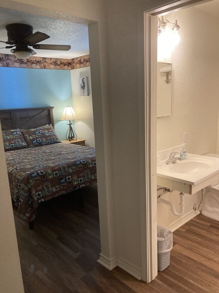 Bedroom and bathroom connected by doorway. Bedroom has bed, blue wall, and lamp. Bathroom has sink.