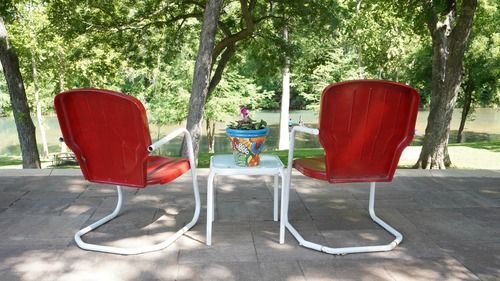Two red chairs face a small table with a flower pot on an outdoor deck.
