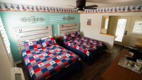 Two double beds in a western-themed motel room, with red, white, and blue quilt covers and rustic headboards.