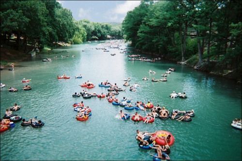 People floating on inner tubes in a turquoise river, surrounded by trees.