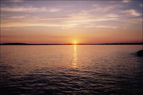 Sunset over calm water, with orange and purple hues reflecting on the surface.
