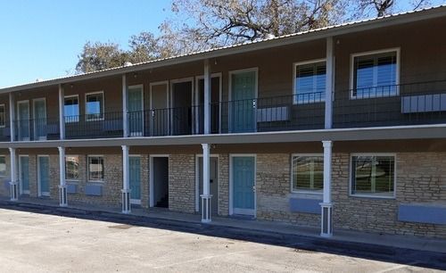 Two-story beige motel with light blue doors and windows under a clear sky.