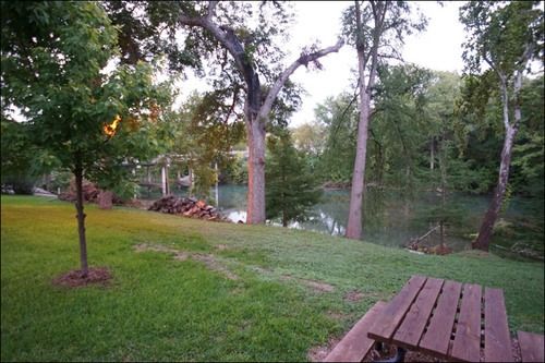 Lawn with a picnic table overlooking a river bordered by trees.