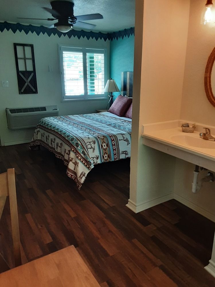 Bedroom with bed, window, and bathroom with a sink. Dark wood floor, teal walls, decorative border.