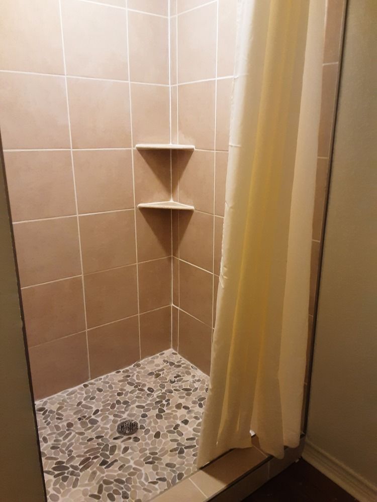 Shower stall with brown tile walls and pebble floor, beige shower curtain.