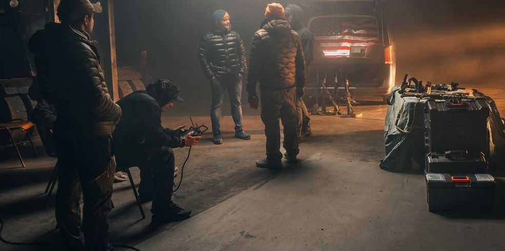 Stunt coordinator Ferdi is captured in a side view, holding a monitor in one hand while he intently watches the action displayed on the screen.