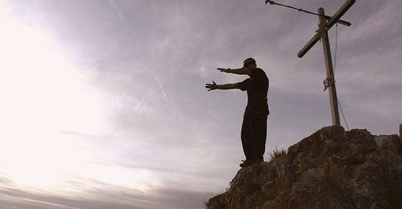 Ferdi Fischer standing seconds before the 45 meter Burgsteinfelsen gainer in Dollnstein Bavaria, positioned under the wooden cross at the cliff edge just before the jump
