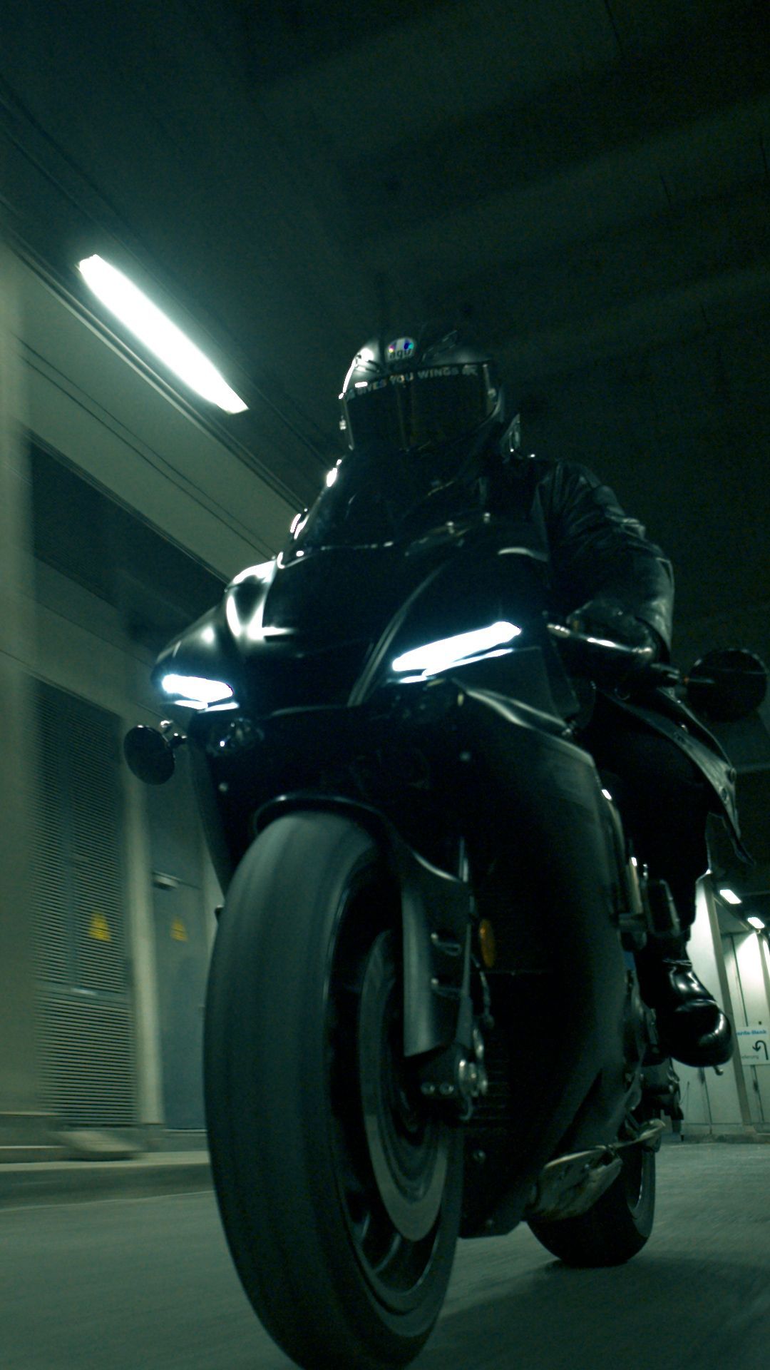 Low-angle 45 degree WarpCam still of a black-clad rider on a motorcycle speeding through a tunnel, captured close to the front wheel at high speed for a cinematic commercial look.