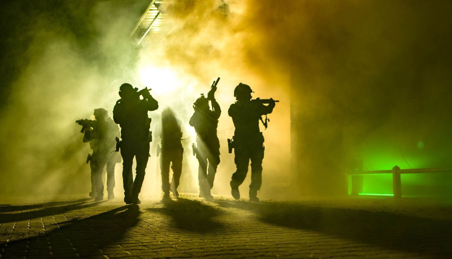 Image of military operators in combat uniforms appearing from a dense smokescreen, equipped with tactical gear and weapons, ready for action.