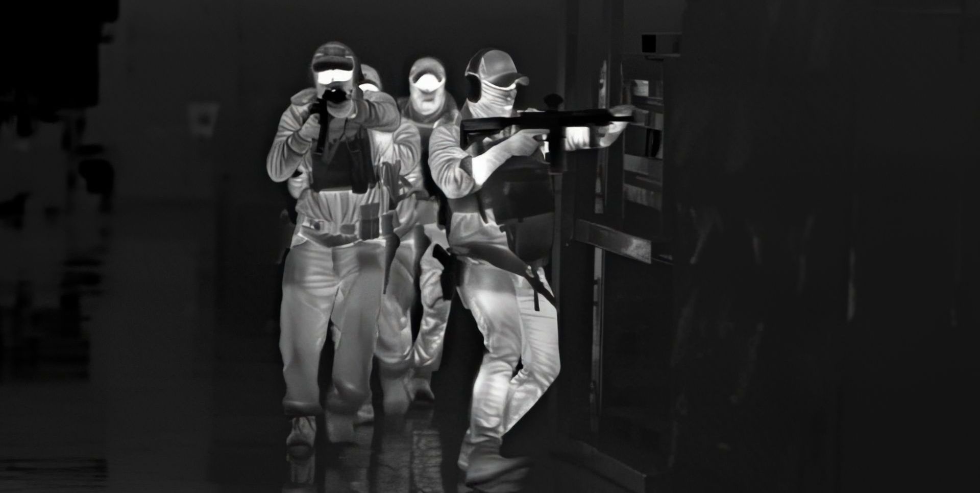 Alternate angle thermal image capturing tactical operators in full gear as they methodically clear a facility, highlighted by distinct heat signatures.