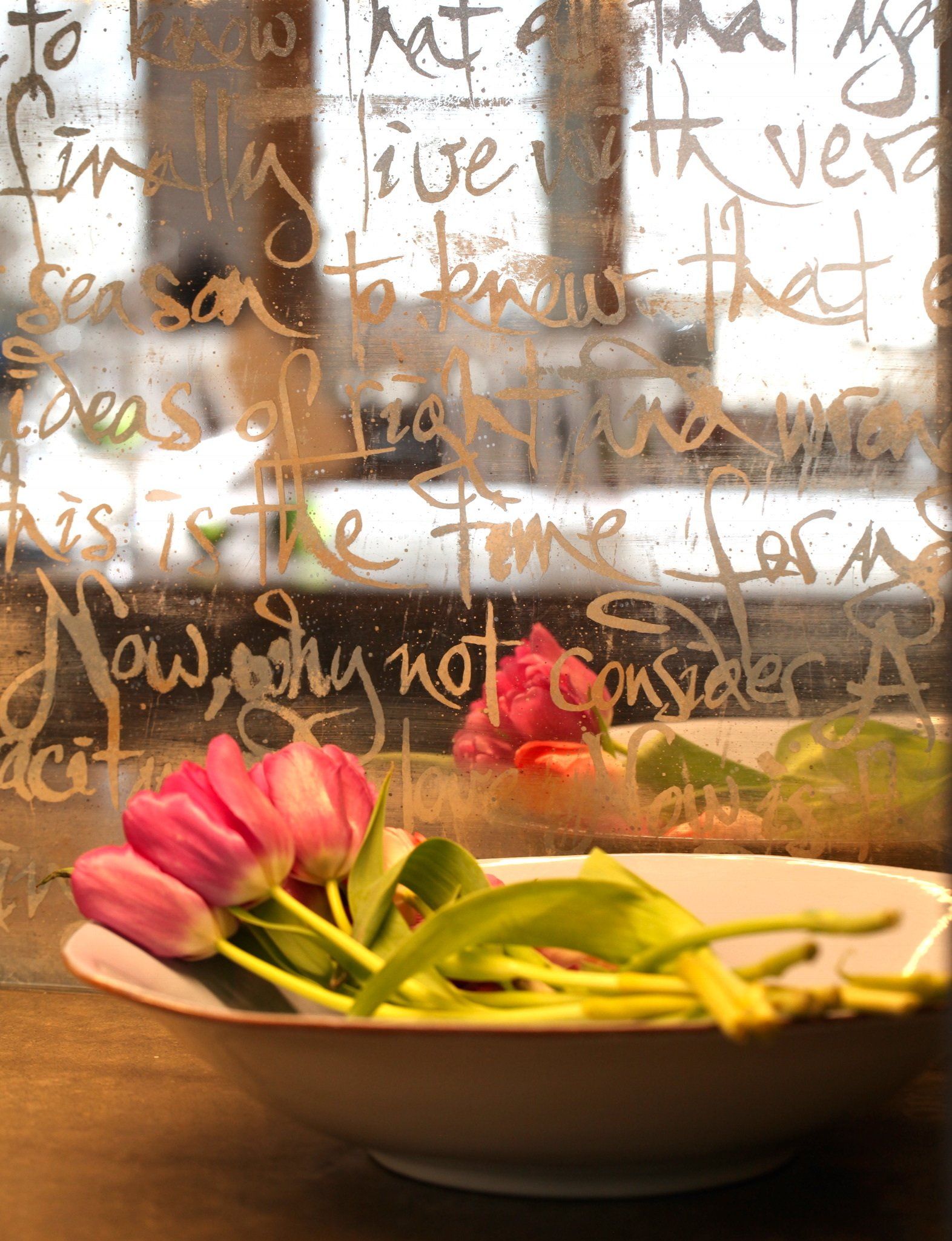 A bowl of flowers sits in front of a window with writing on it
