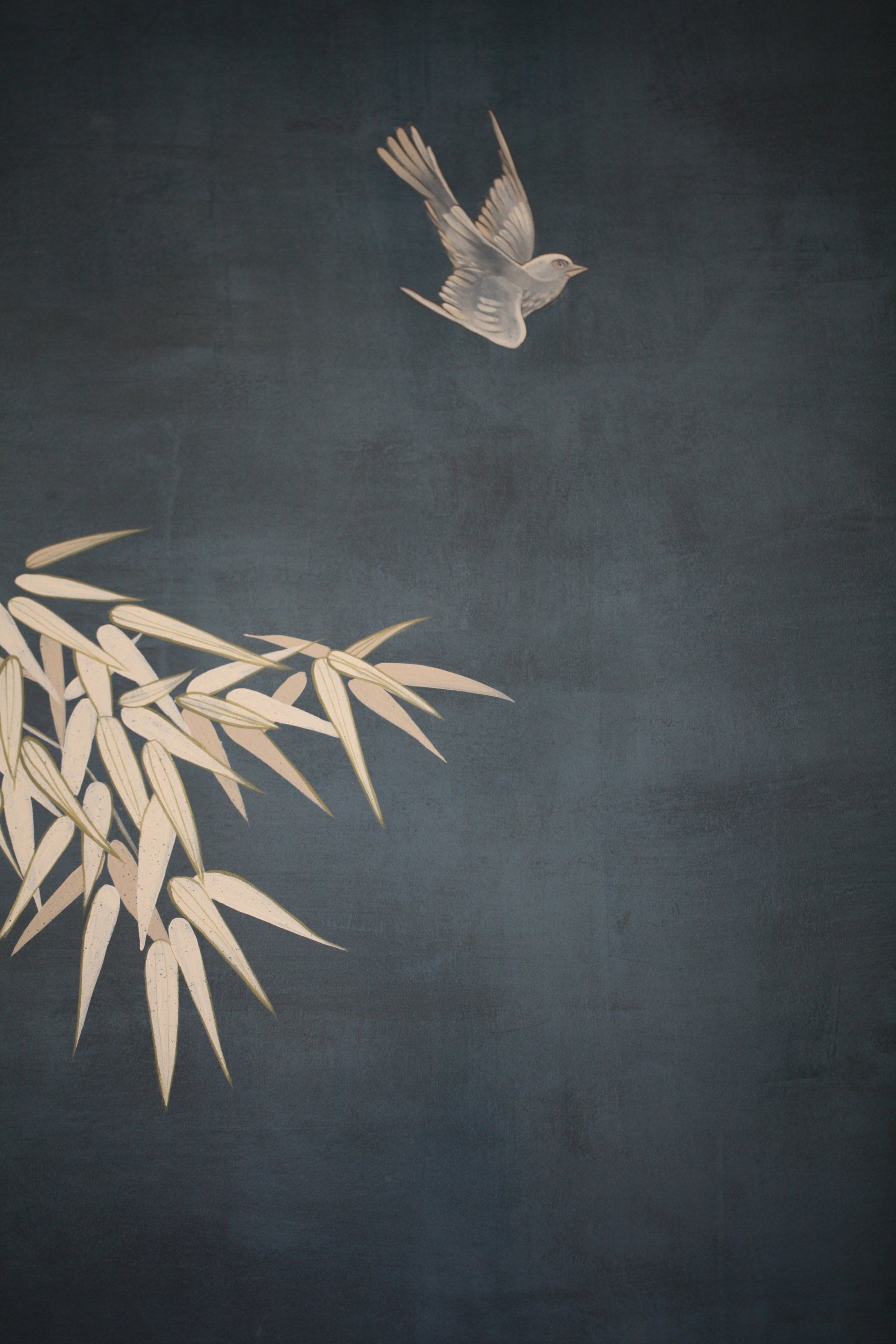 A bird is flying over a branch of bamboo.