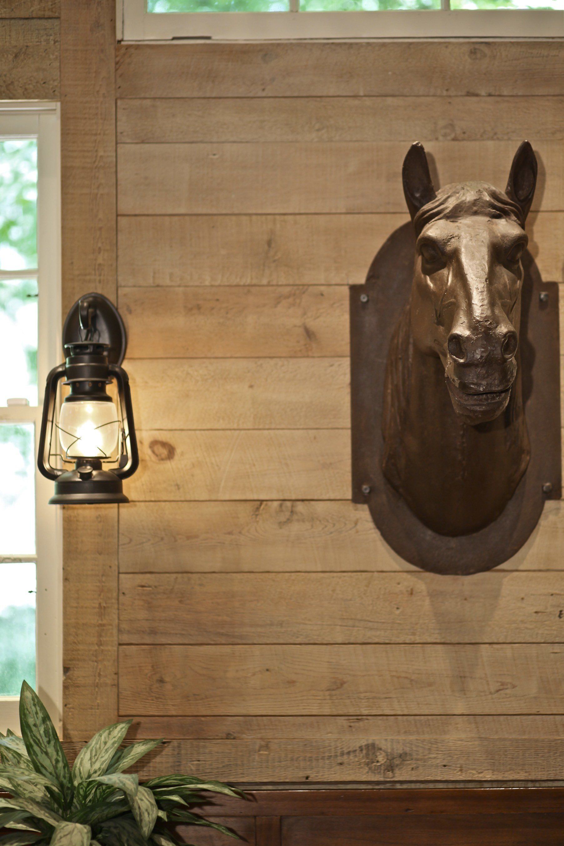 A horse head is hanging on a wooden wall next to a lantern.