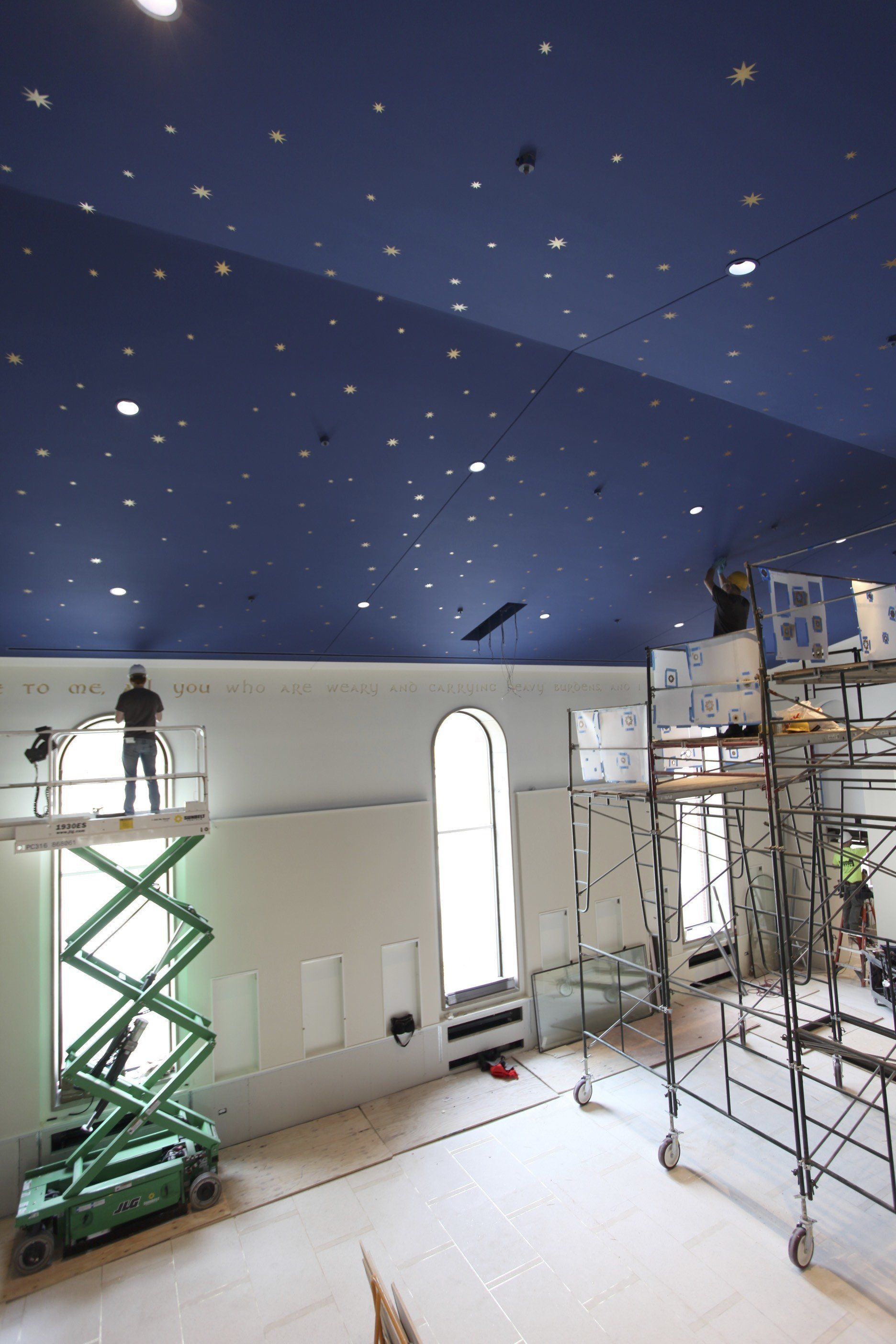 A man is standing on a scissor lift in a room with a blue ceiling.