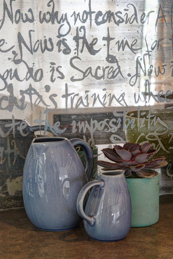 Three vases are sitting on a table in front of a wall with graffiti on it.