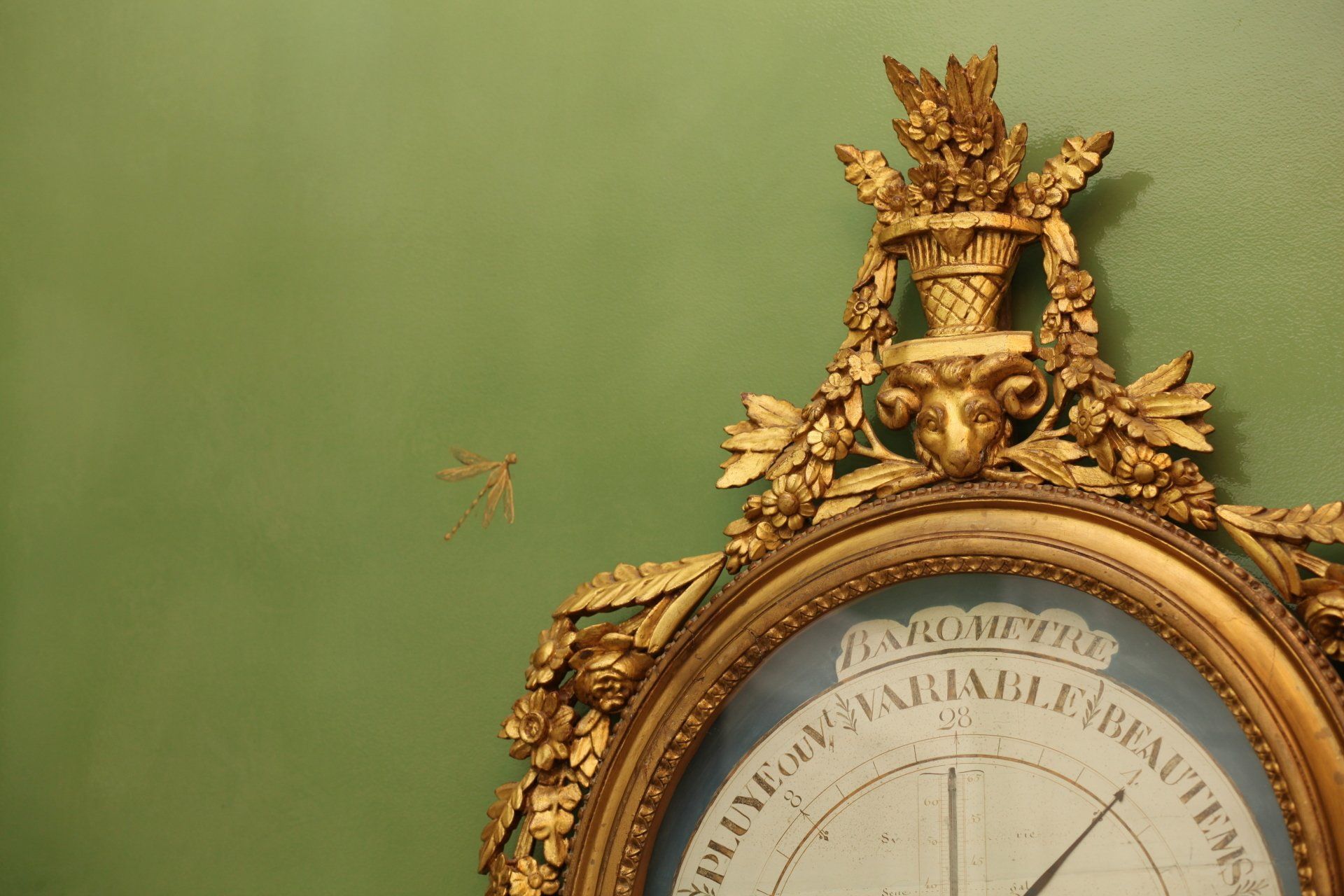 A clock with a gold frame is hanging on a green wall