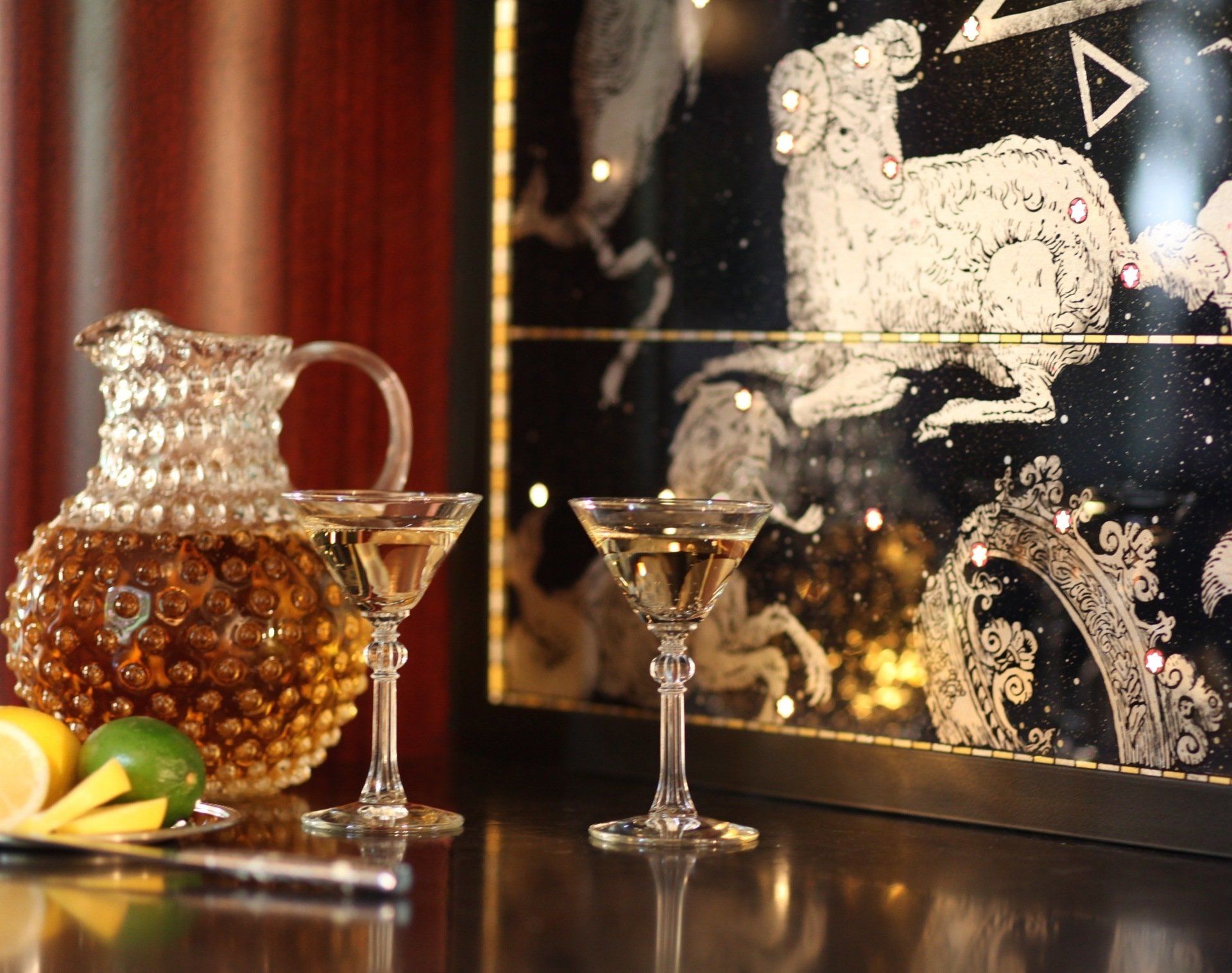 Two martini glasses are sitting on a bar next to a pitcher of pineapple slices.